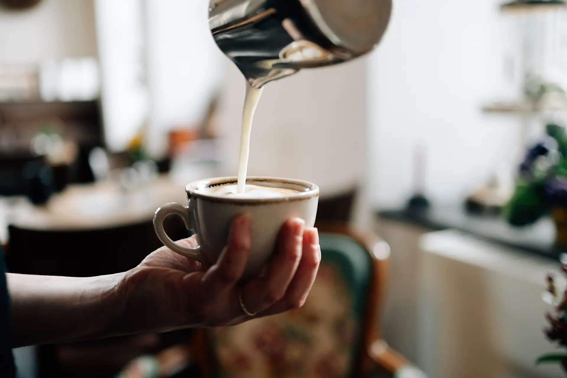 Milch wird in eine Tasse Kaffee gegossen